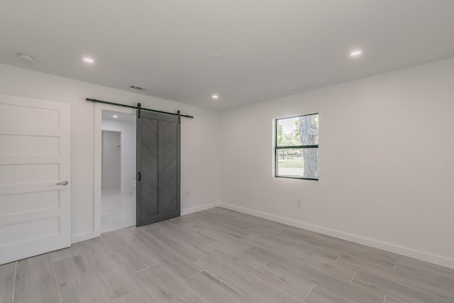 13516 Spring Grove Ave, Dallas, TX 75240 - unfurnished bedroom featuring a barn door, light wood-style floors, and recessed lighting
