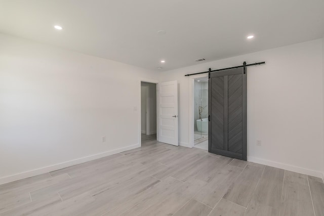13516 Spring Grove Ave, Dallas, TX 75240 - unfurnished bedroom featuring a barn door, light wood finished floors, recessed lighting, and ensuite bathroom