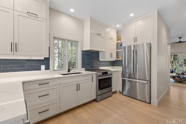 kitchen with appliances with stainless steel finishes, light stone counters, white cabinets, light hardwood / wood-style floors, and sink