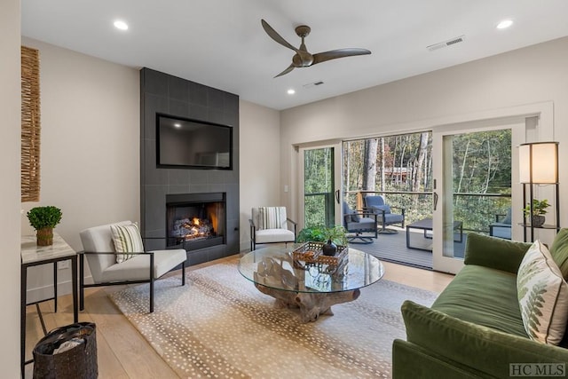 living room with ceiling fan, light hardwood / wood-style flooring, and a large fireplace