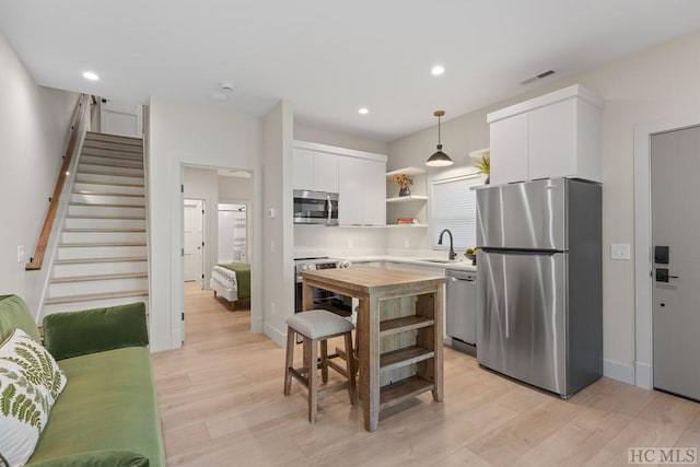 kitchen with white cabinetry, light wood-type flooring, stainless steel appliances, a center island, and decorative light fixtures