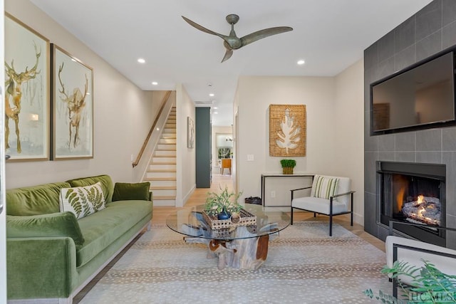 living room with a fireplace, ceiling fan, and light wood-type flooring