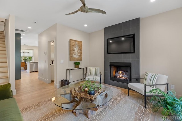 living room with light wood-type flooring, a tiled fireplace, and ceiling fan