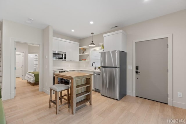 kitchen featuring hanging light fixtures, light hardwood / wood-style flooring, sink, appliances with stainless steel finishes, and white cabinets