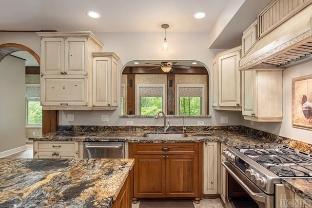 kitchen featuring sink, appliances with stainless steel finishes, custom range hood, pendant lighting, and dark stone counters