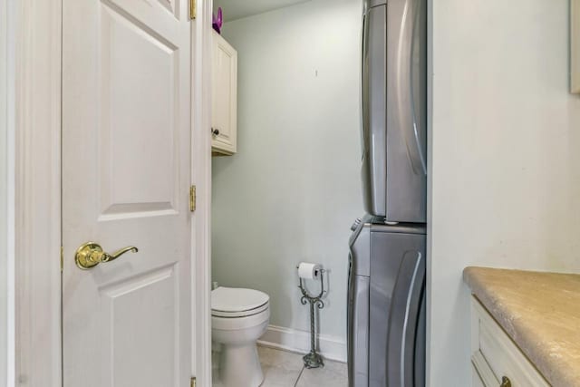 bathroom with estacked washer and dryer, toilet, tile patterned flooring, and baseboards