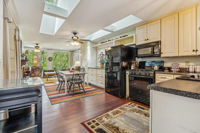 kitchen featuring a skylight, black appliances, cream cabinets, dark wood-style flooring, and dark countertops