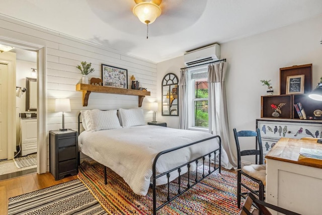 bedroom featuring a wall mounted air conditioner, wood finished floors, connected bathroom, and a ceiling fan