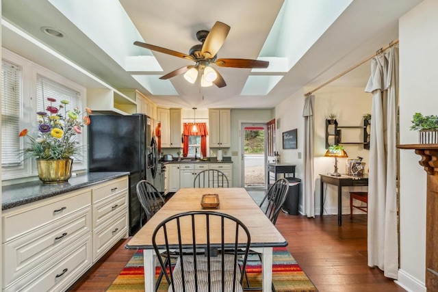 dining space featuring a skylight, ceiling fan, dark wood-style floors, and baseboards