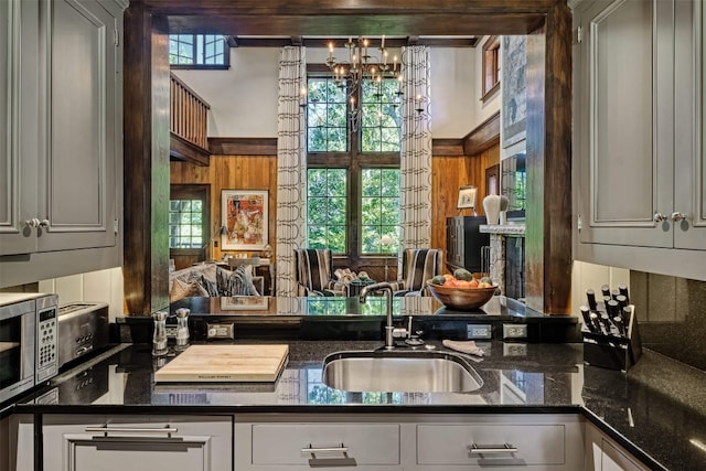 kitchen featuring a sink, wood walls, stainless steel microwave, and dark stone countertops