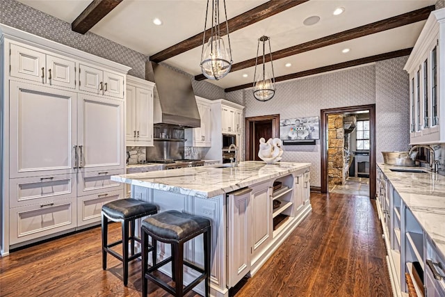 kitchen featuring dark wood-style flooring, wallpapered walls, a sink, and wall chimney exhaust hood