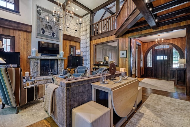 living area featuring wooden walls, a high ceiling, an inviting chandelier, a stone fireplace, and beamed ceiling