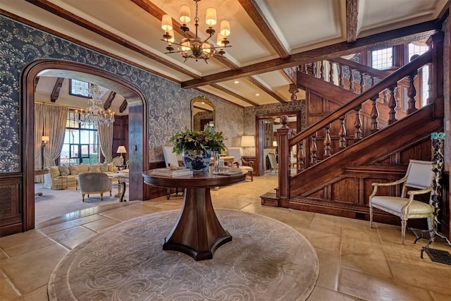 entryway featuring arched walkways, stairs, beamed ceiling, a notable chandelier, and wallpapered walls