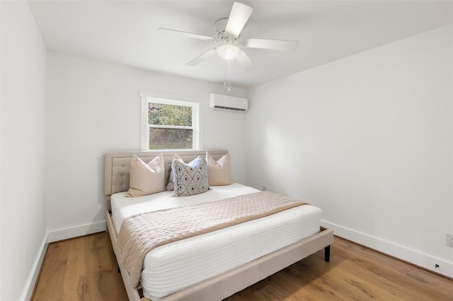bedroom featuring baseboards, a wall mounted air conditioner, ceiling fan, and wood finished floors