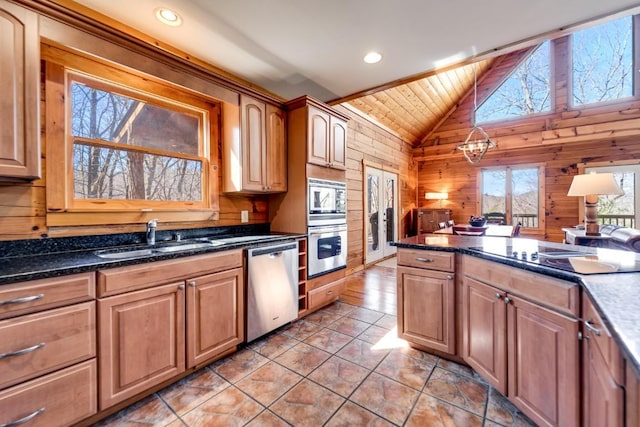 kitchen with wooden walls, lofted ceiling, appliances with stainless steel finishes, hanging light fixtures, and a sink