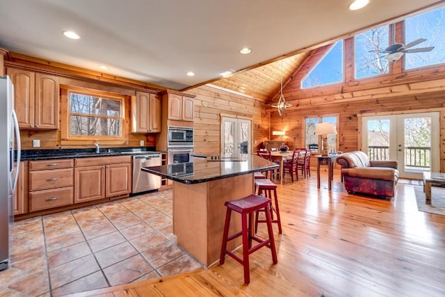 kitchen with appliances with stainless steel finishes, open floor plan, a center island, wood walls, and a kitchen bar