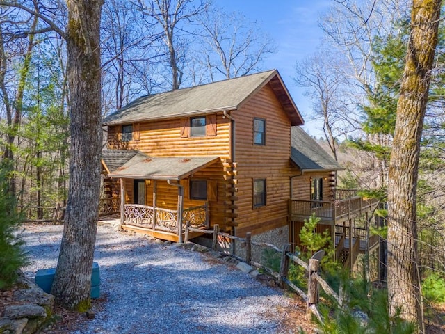 log-style house with covered porch, driveway, and log siding