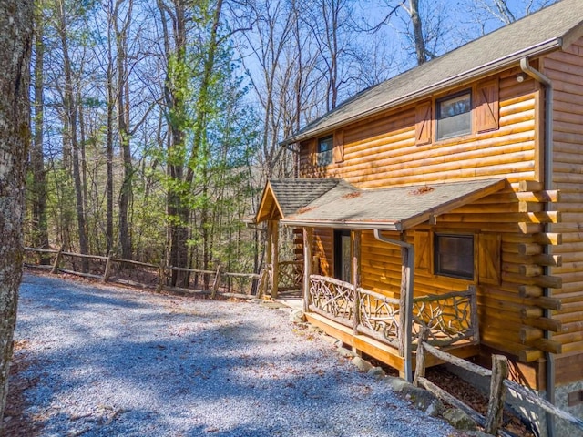 view of side of property featuring driveway, log exterior, roof with shingles, fence, and a porch