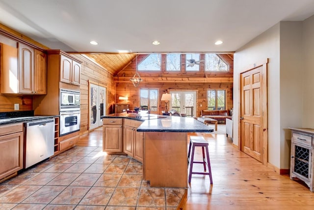 kitchen with wooden walls, a kitchen island, appliances with stainless steel finishes, a breakfast bar area, and vaulted ceiling