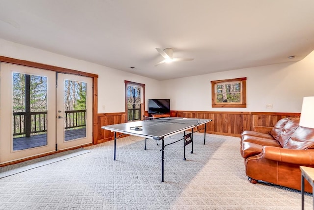 game room featuring wooden walls, light colored carpet, wainscoting, ceiling fan, and french doors