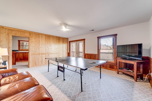 recreation room with french doors, a wainscoted wall, visible vents, light carpet, and wood walls