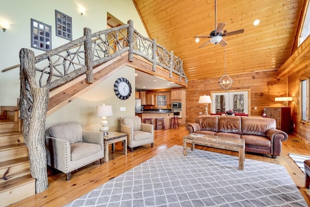 living area with a towering ceiling, light wood-style floors, wood walls, wooden ceiling, and stairs