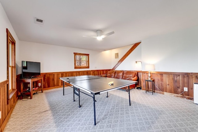 rec room with light carpet, a wainscoted wall, wooden walls, and a ceiling fan