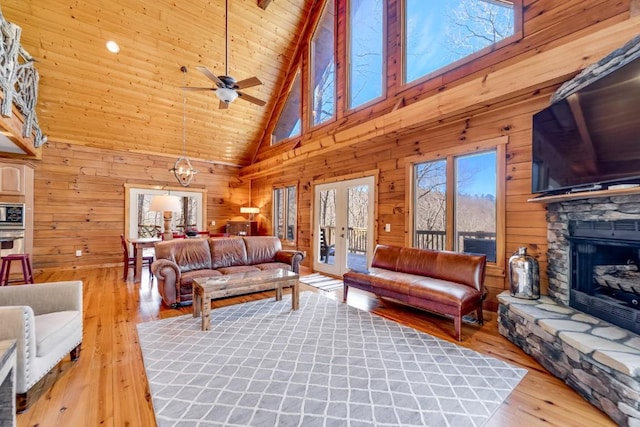 living area with wood walls, light wood finished floors, french doors, and a stone fireplace