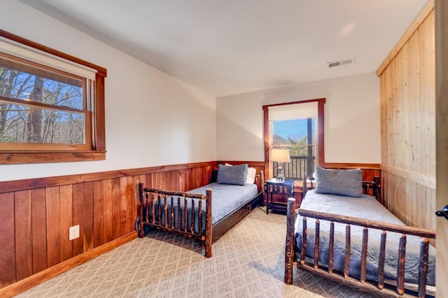 bedroom featuring light carpet, wainscoting, visible vents, and wooden walls