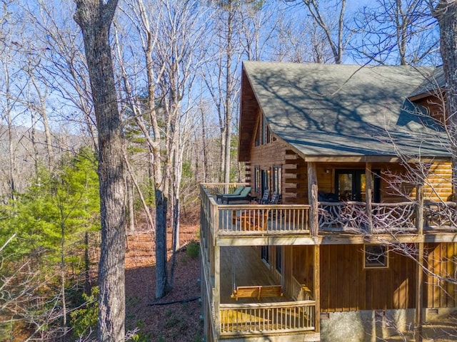 view of side of property with a shingled roof, a wooden deck, and log siding