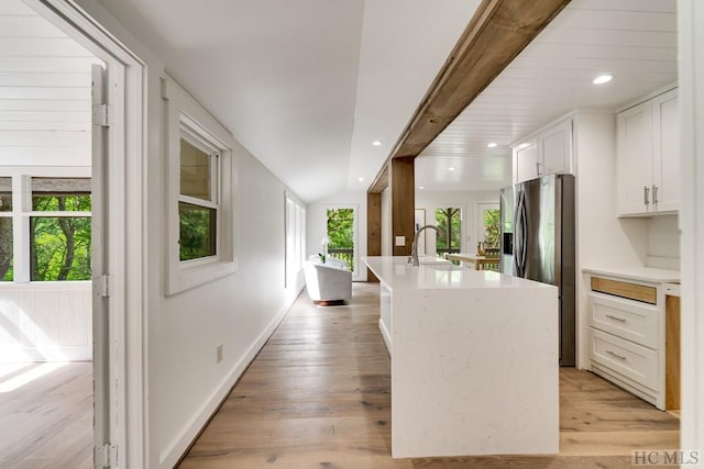 kitchen featuring light hardwood / wood-style flooring, white cabinetry, stainless steel refrigerator with ice dispenser, a healthy amount of sunlight, and a center island with sink