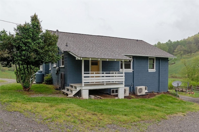 ranch-style home featuring roof with shingles, concrete block siding, ac unit, and a front lawn