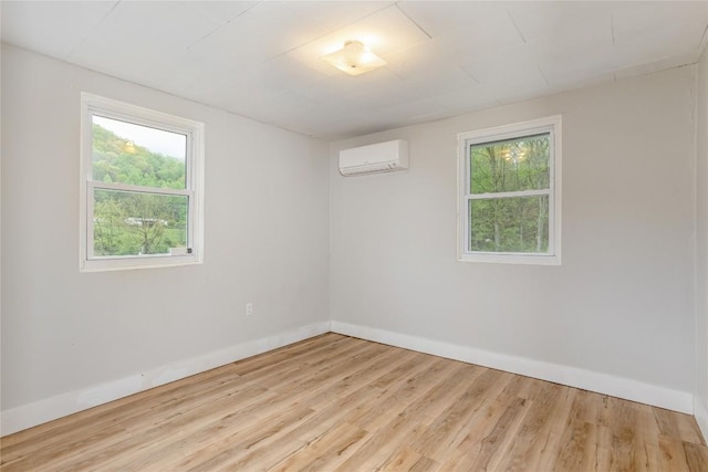 unfurnished room featuring wood finished floors, baseboards, a wall mounted air conditioner, and a wealth of natural light