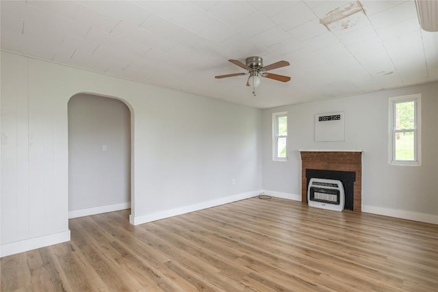 unfurnished living room featuring heating unit, a brick fireplace, light wood-type flooring, arched walkways, and a ceiling fan