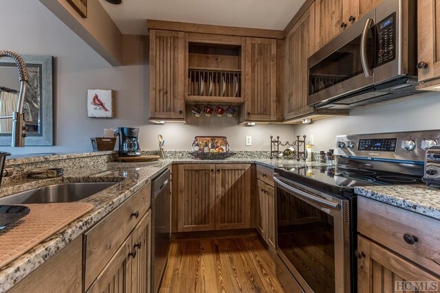 kitchen with light stone counters, stainless steel appliances, sink, and light wood-type flooring