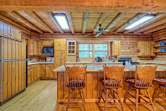 kitchen with black appliances, a kitchen bar, light hardwood / wood-style floors, wooden ceiling, and rustic walls