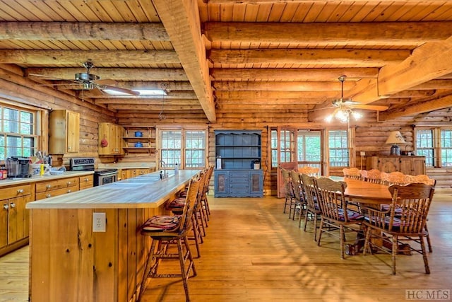 kitchen featuring wooden ceiling, stainless steel electric range oven, rustic walls, beam ceiling, and a healthy amount of sunlight