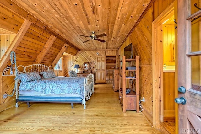 bedroom featuring light hardwood / wood-style floors, connected bathroom, wood walls, and vaulted ceiling