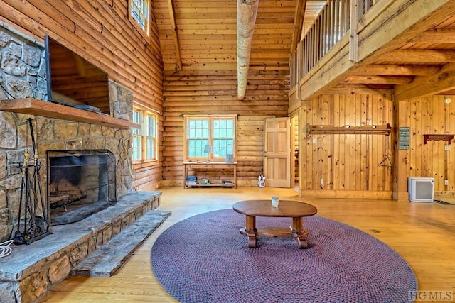 living room with log walls, a fireplace, wood walls, high vaulted ceiling, and light hardwood / wood-style flooring