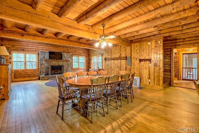 dining room with wood ceiling, a stone fireplace, beamed ceiling, and a healthy amount of sunlight