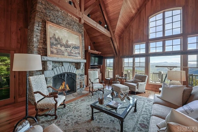 living room featuring hardwood / wood-style flooring, beam ceiling, a towering ceiling, a stone fireplace, and wooden ceiling