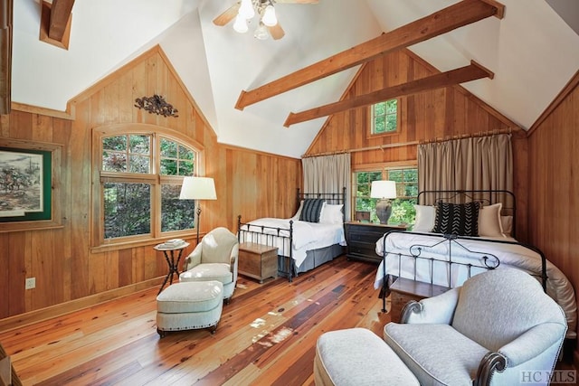 bedroom featuring beam ceiling, wood-type flooring, wooden walls, and ceiling fan