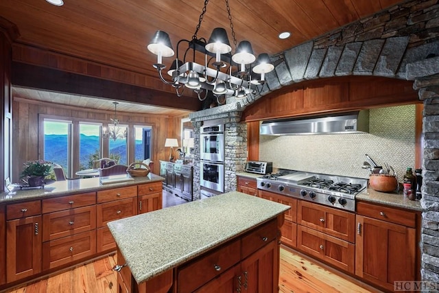 kitchen featuring an inviting chandelier, appliances with stainless steel finishes, decorative light fixtures, and wall chimney range hood