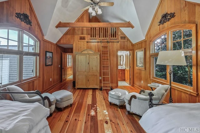 bedroom featuring high vaulted ceiling, light wood-type flooring, wooden walls, beamed ceiling, and ceiling fan