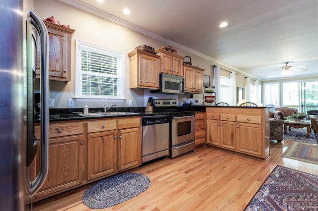 kitchen featuring kitchen peninsula, stainless steel appliances, light wood-type flooring, ornamental molding, and sink