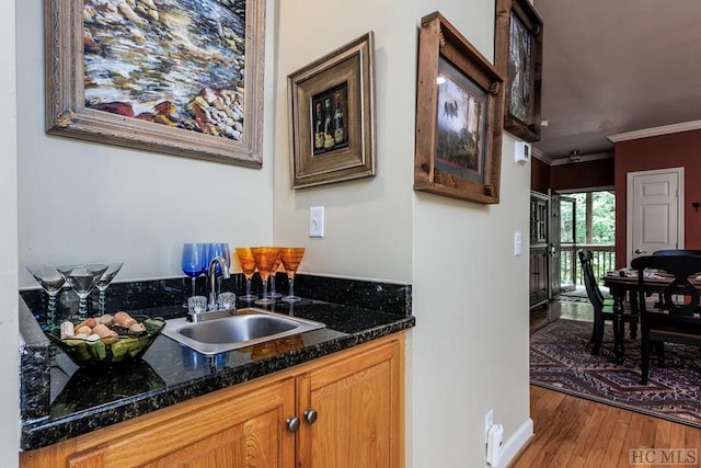 interior space with sink, wood-type flooring, ornamental molding, and dark stone countertops