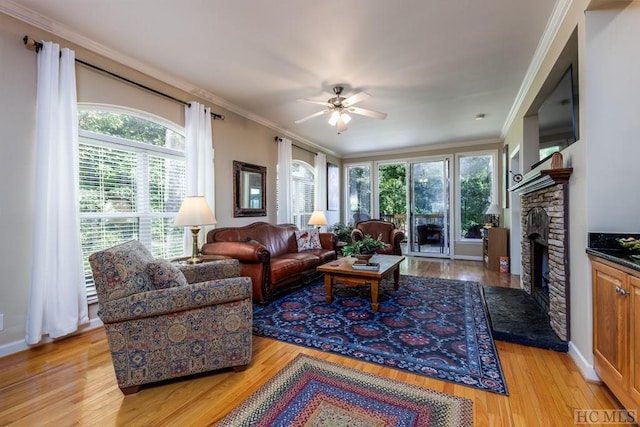 living room featuring light hardwood / wood-style floors, ceiling fan, ornamental molding, and a stone fireplace