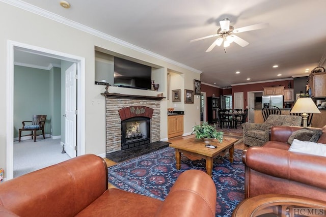 carpeted living room with ceiling fan, crown molding, and a stone fireplace