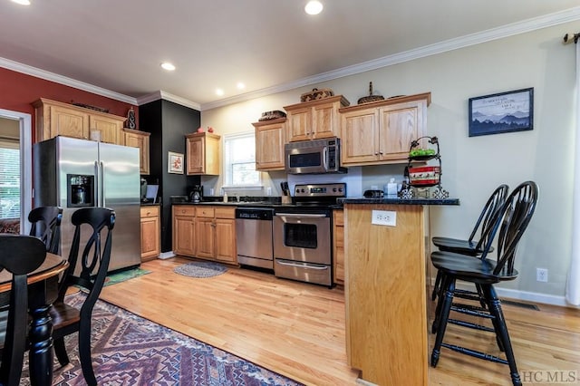 kitchen featuring light wood-type flooring, crown molding, stainless steel appliances, and a kitchen bar