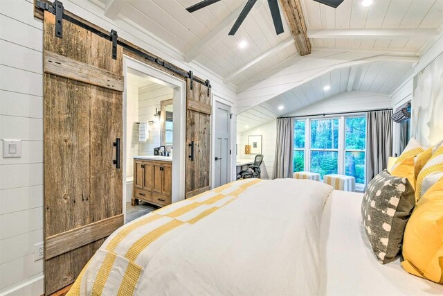 bedroom featuring ensuite bathroom, wooden walls, vaulted ceiling with beams, a barn door, and recessed lighting